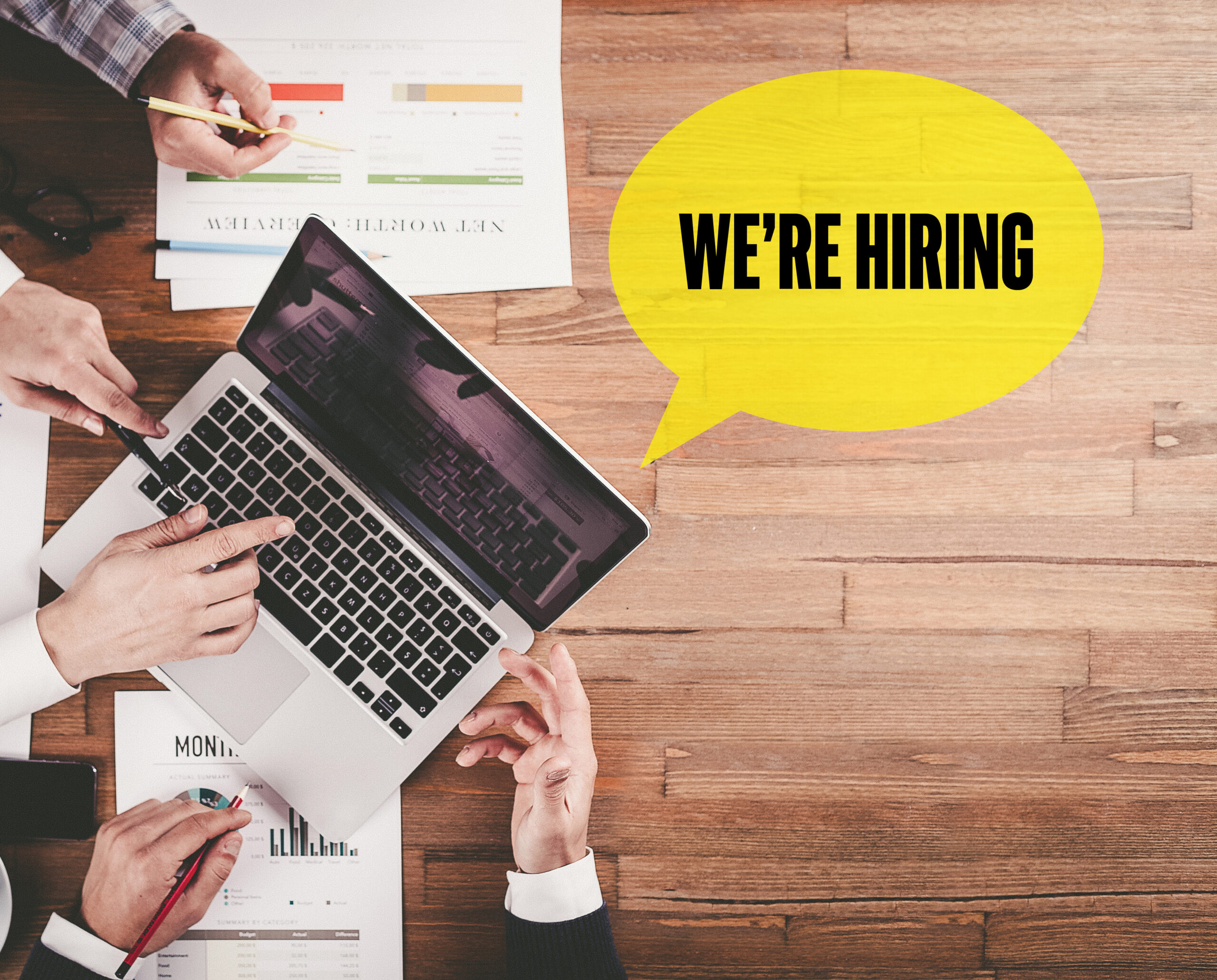 BUSINESS TEAM WORKING IN OFFICE WITH WE'RE HIRING SPEECH BUBBLE BUSINESS TEAM WORKING IN OFFICE WITH WE'RE HIRING SPEECH BUBBLE ON DESK